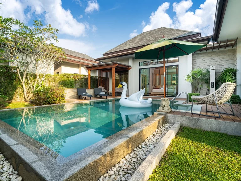 Backyard pool with landscaping, chairs, an umbrella, and a swan floatie.