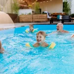 Multi generation family having fun and enjoying swimming in backyard pool during summer holiday.