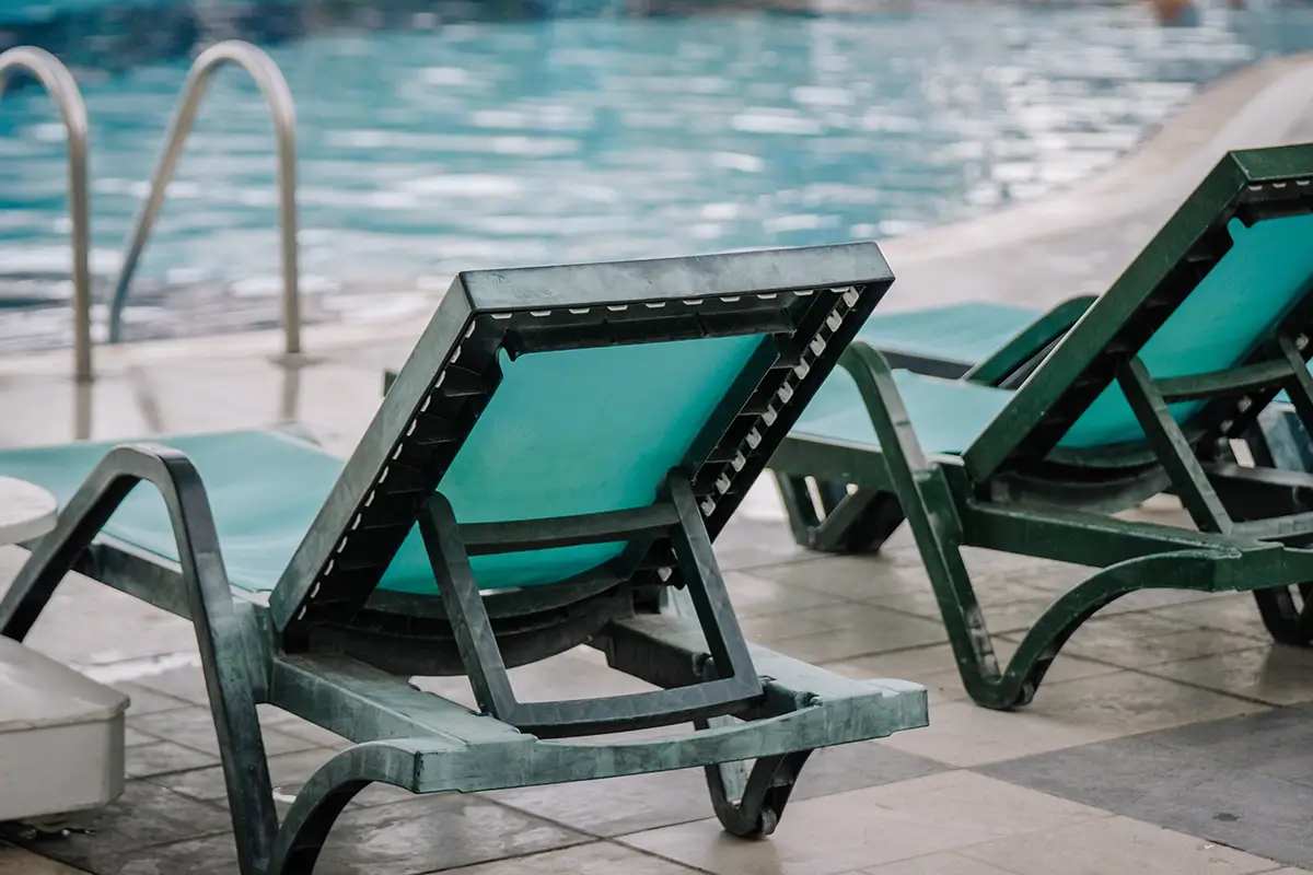 Close up of the back side of a green pool chair facing the pool