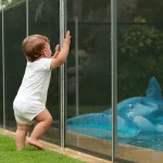 Baby leaning on swimming pool fence protection.