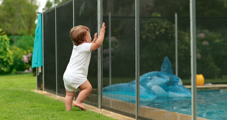 Baby leaning on swimming pool fence protection.