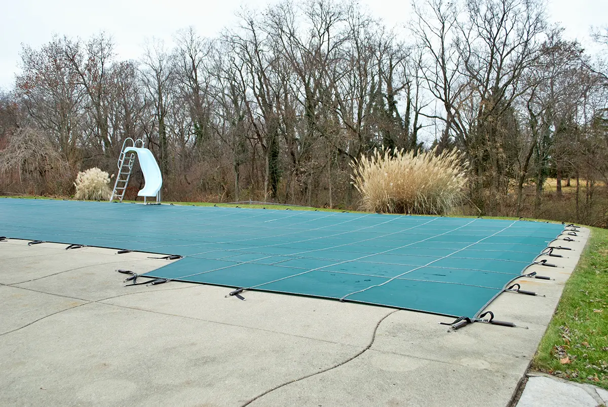 backyard swimming pool with pool slide tarped up and closed down for winter